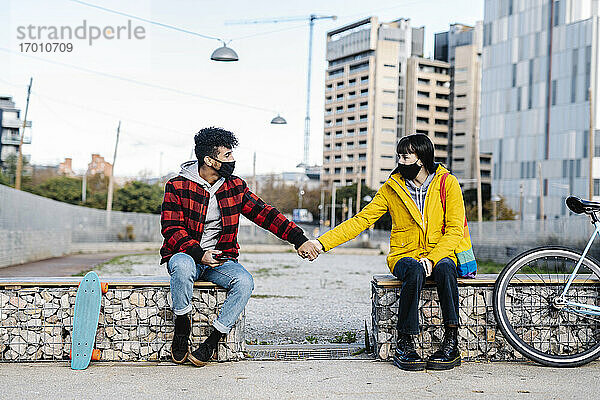 Paar mit Gesichtsschutzmaske hält sich auf einer Bank sitzend an den Händen