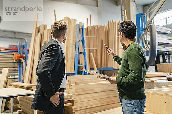 Zwei Zimmerleute im Gespräch vor gestapelten Holzbrettern in einer Produktionshalle