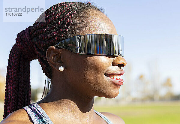 Glückliche Sportlerin mit Sonnenbrille  die an einem sonnigen Tag in den klaren Himmel schaut