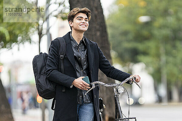 Lächelnder gut aussehender junger Mann  der in der Stadt Fahrrad fährt
