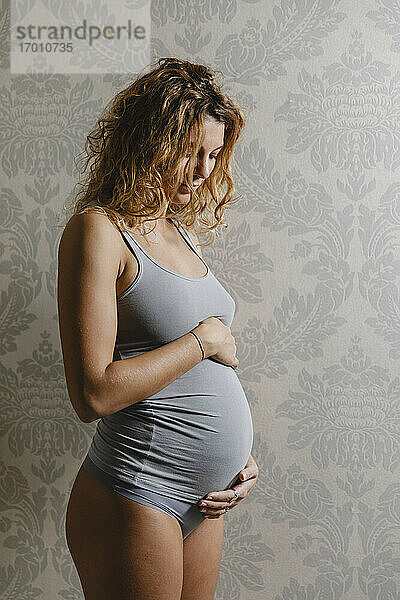 Junge Schwangere  die zu Hause ihren Unterleib an die Wand drückt