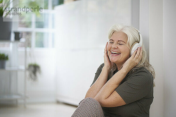 Glückliche ältere Frau  die in ihrer Wohnung Musik über Kopfhörer hört