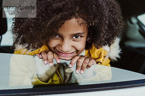 Nahaufnahme eines lächelnden Mädchens mit lockigem Haar  das durch ein Autofenster schaut