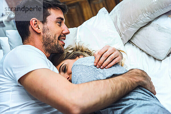 Glückliches zärtliches junges Paar kuschelt zu Hause im Bett