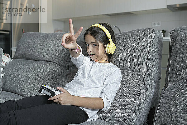Kleines Mädchen macht Friedenszeichen  während sie im Wohnzimmer ein Videospiel spielt