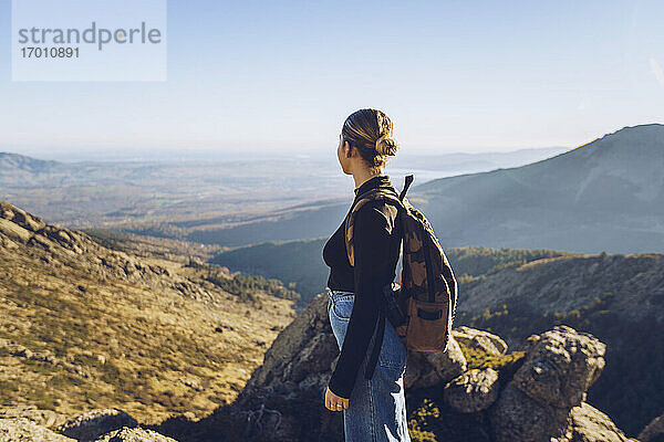 Weiblicher Wanderer mit Rucksack  der auf dem Gipfel eines Berges steht und die Aussicht betrachtet