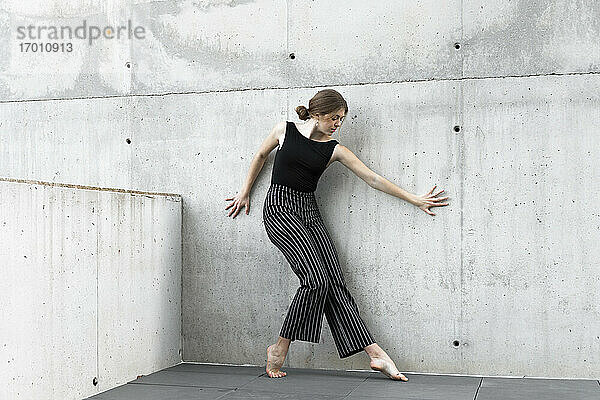 Tänzerin in schwarzer gestreifter Hose vor einer Betonwand