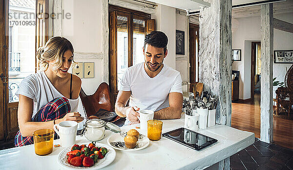 Junges Paar sitzt am Tisch und frühstückt zu Hause