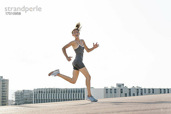 Glückliche Sportlerin beim Laufen gegen den klaren Himmel in der Stadt