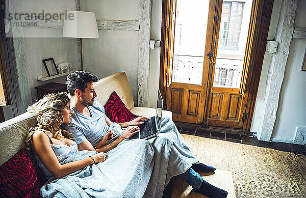 Junges Paar sitzt zu Hause auf der Couch und beobachtet den Laptop