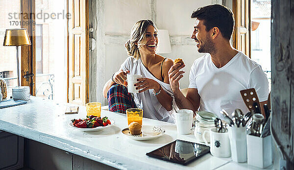 Glückliches junges Paar sitzt am Tisch und frühstückt zu Hause