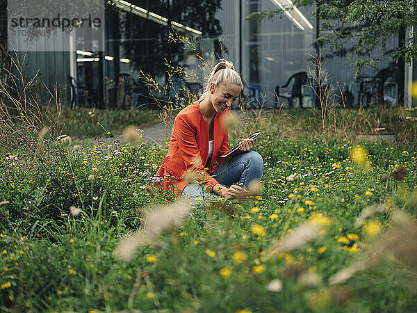 Lächelnde Geschäftsfrau betrachtet Blumen im Firmengarten