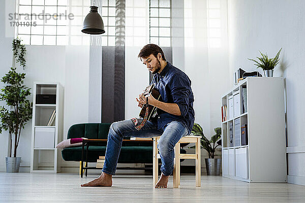 Profi bei einer Probe mit Gitarre auf einem Hocker im Studio sitzend