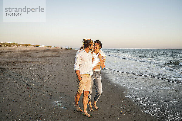 Junges Paar spaziert am Strand gegen den klaren Himmel im Urlaub