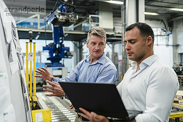 Männlicher Vorgesetzter schaut Manager an  während er in einer Besprechung in einer Fabrik einen Laptop benutzt