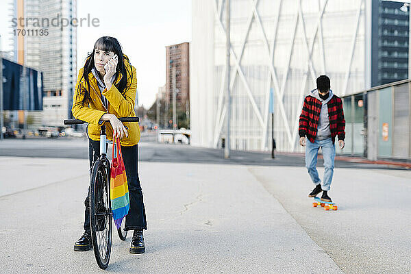 Frau  die mit einem Mobiltelefon spricht  während ihr Freund im Hintergrund Skateboard fährt