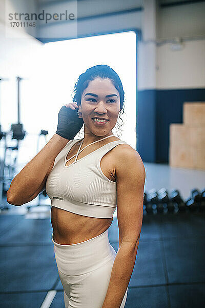 Lächelnde Sportlerin mit Hand im Haar träumt im Fitnessstudio
