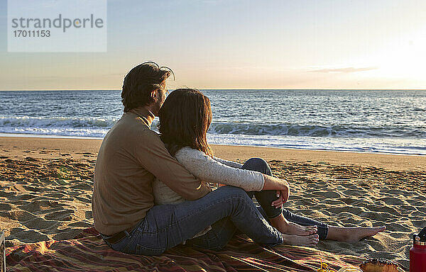 Junges Paar mit Blick auf das Meer am Strand sitzend