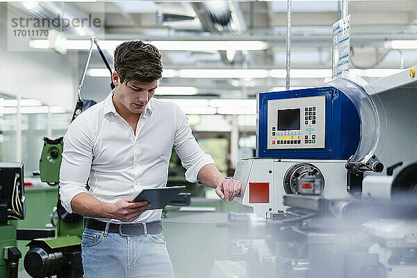 Männlicher Fachmann  der ein digitales Tablet benutzt  während er an einem Maschinenpark in der Industrie steht