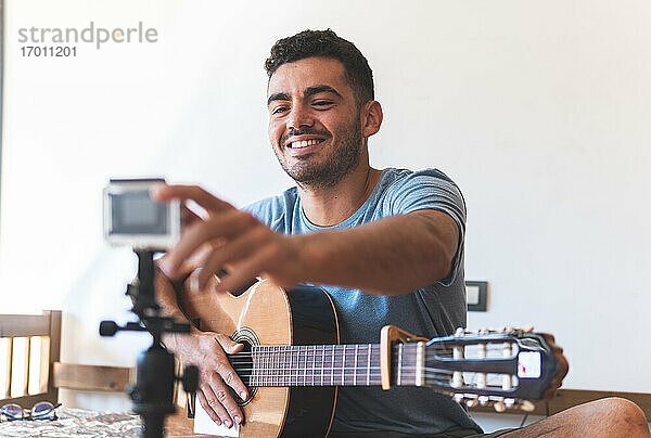 Lächelnder männlicher Musiker  der zu Hause durch die Kamera vloggt