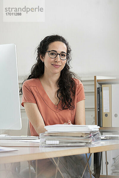 Weibliche Fachkraft lächelt  während sie am Schreibtisch im Büro sitzt