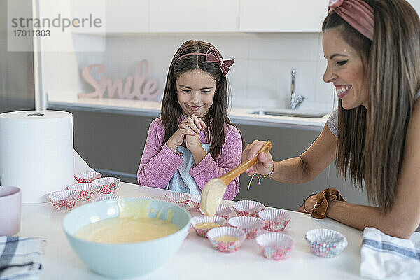 Mutter schöpft Teig in Muffinhalter durch Tochter in Küche