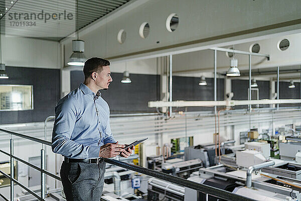 Geschäftsmann mit digitalem Tablet mit Blick auf eine Fabrikhalle