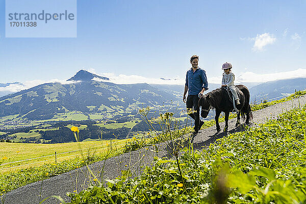 Vater geht neben seiner kleinen Tochter  die auf einem Pony reitet  einen alpinen Wanderweg entlang