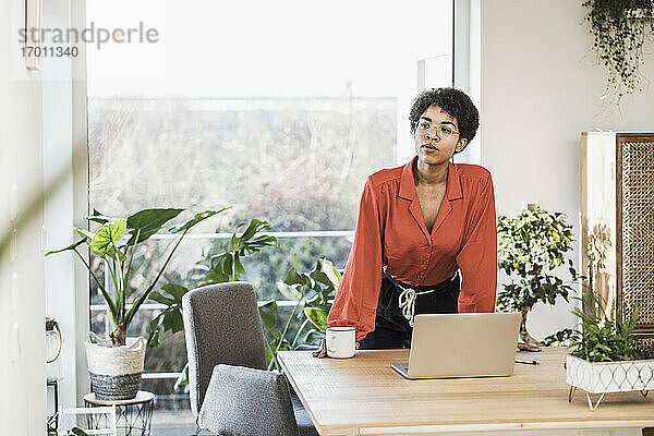 Frau stehend am Tisch mit Laptop zu Hause