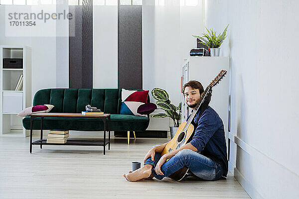 Musiker lächelt  während er mit seiner Gitarre auf dem Boden im Studio sitzt