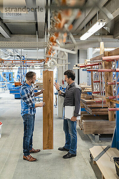 Zwei Zimmerleute inspizieren Holzbretter in der Produktionshalle