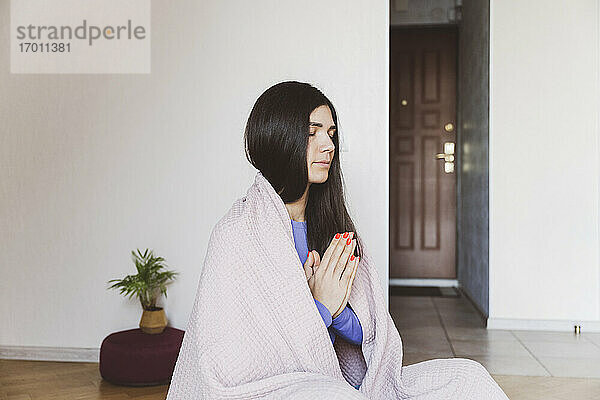 In eine Decke gehüllte Frau  die zu Hause sitzt und meditiert