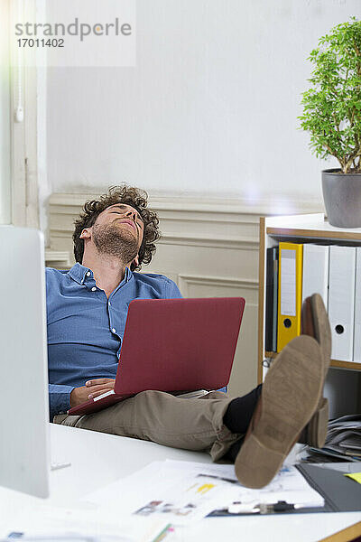 Männlicher Unternehmer entspannt mit Laptop im Büro