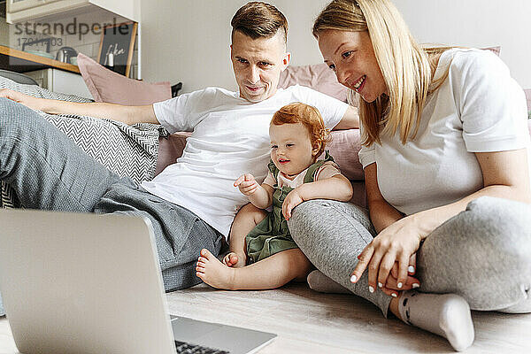 Glückliche Familie mit kleiner Tochter  die zu Hause auf den Laptop schaut