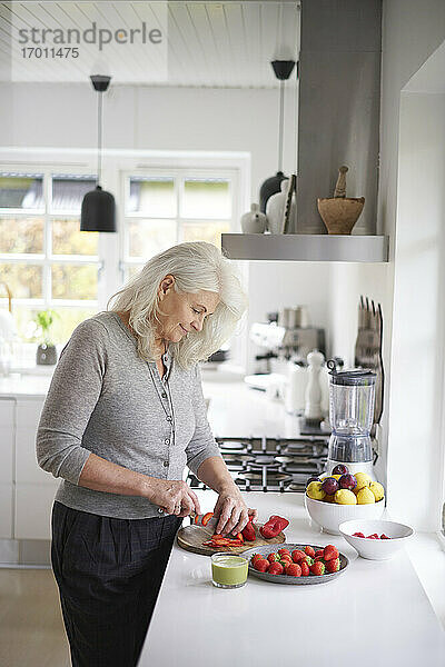 Ältere Frau im Ruhestand schneidet Erdbeeren in der Küche zu Hause