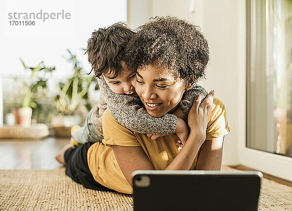 Lächelnde Mutter mit ihrem Sohn  der ein digitales Tablet benutzt  während er zu Hause liegt