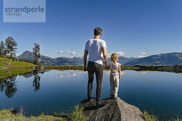 Vater steht mit seiner kleinen Tochter auf einem Felsen am Seeufer