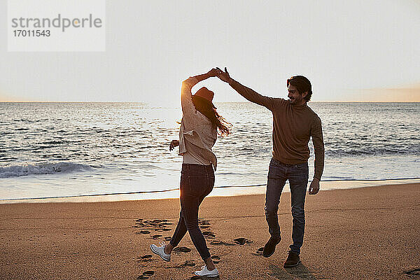 Glückliches junges Paar  das bei Sonnenaufgang am Strand tanzt