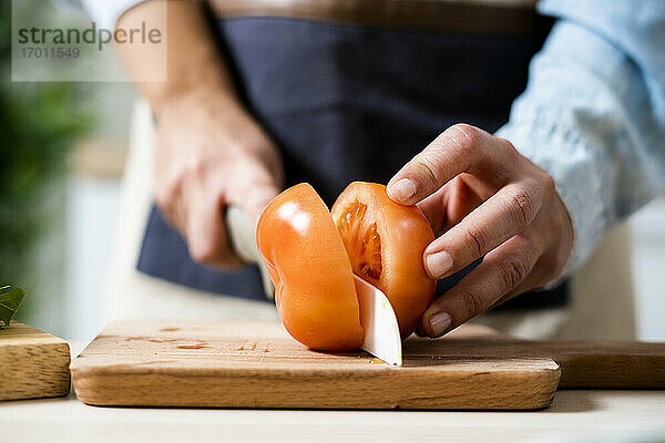 Die Hände einer Frau  die eine Tomate auf einem Schneidebrett schneidet