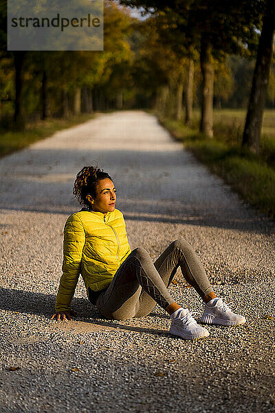 Weibliche Athletin ruht sich bei Sonnenuntergang auf der Straße sitzend aus