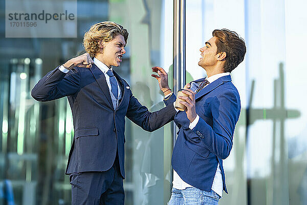 Wütender junger Geschäftsmann streitet mit einem männlichen Kollegen vor einem Bürogebäude