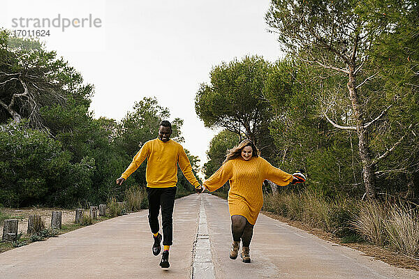 Unbekümmertes Paar hält sich beim Laufen auf der Straße an den Händen