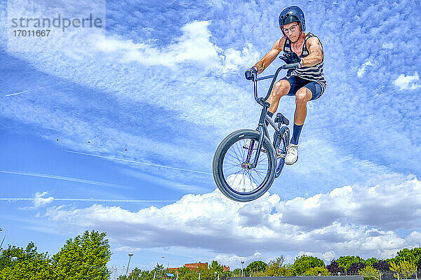 Junger Mann mit Fahrrad springt gegen blauen Himmel im Fahrradpark
