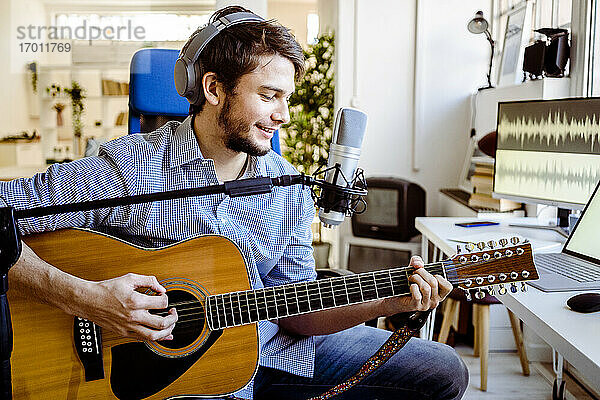 Männlicher Sänger  der im Aufnahmestudio Gitarre spielt und singt