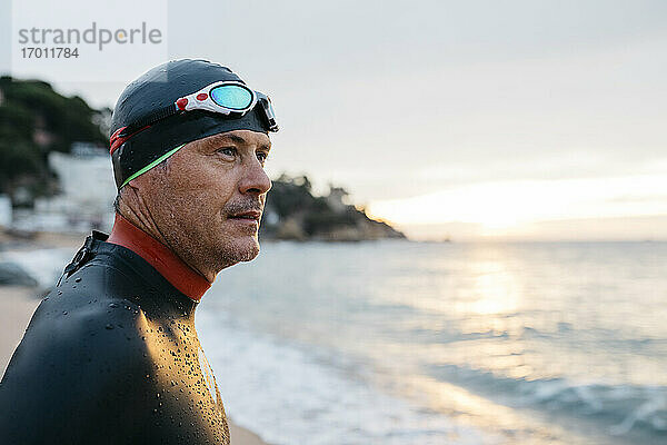 Porträt eines männlichen Schwimmers  der das Meer bei Sonnenuntergang bewundert