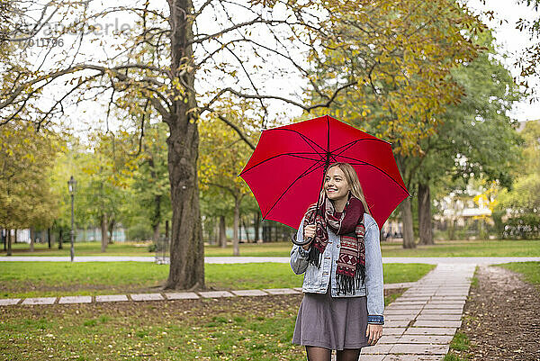 Junge Frau mit Regenschirm geht im Herbst im Park spazieren