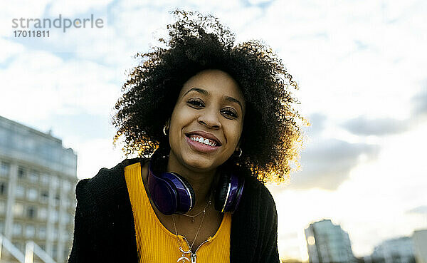 Lächelnde junge Frau mit Afro-Haar gegen den Himmel bei Sonnenuntergang