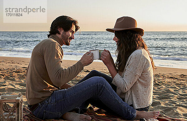 Freundin und Freund Toasting Kaffeetasse beim Sitzen am Strand
