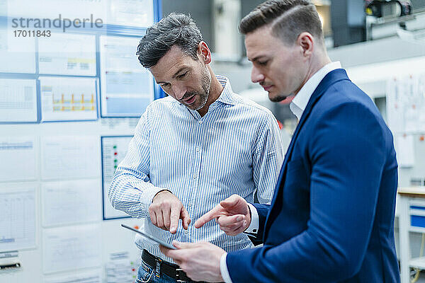 Männliche Mitarbeiter diskutieren in einer Fabrik über ein digitales Tablet die Geschäftsstrategie