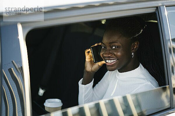 Lächelndes Teenager-Mädchen beim Telefonieren durch das Autofenster gesehen